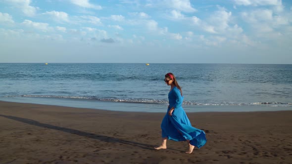 Woman in Beautiful Blue Dress Running Along a Black Volcanic Beach