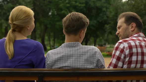 Teenage Son Sitting With Parents on Bench and Talking About Vacation, Trust