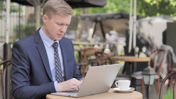 Pensive Businessman Working on Laptop in Outdoor Cafe