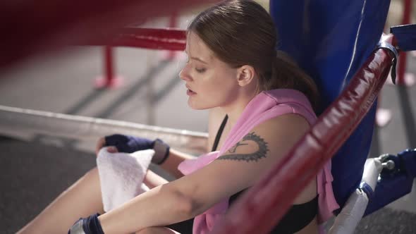 Tired Female Boxer Rubbing Forehead with Towel Drinking Water and Looking at Camera Through Boxing