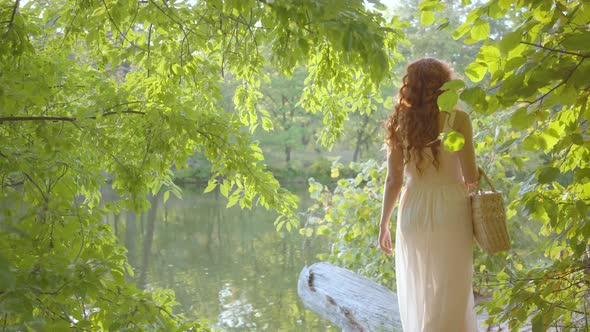 Young Caucasian Woman in Light Dress Walking Through the Forest To the Bank of the Lake. Fairy