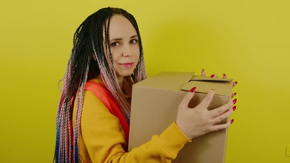 Young Woman in Vest with Cardboard Box on Yellow Background in Studio