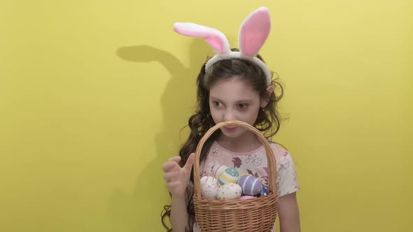 Beautiful Cute Little Girl in Easter Bunny Ears Holds a Basket with Eggs