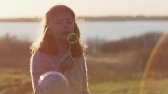 Young Girl Blowing Bubbles Through Wand In Sunset