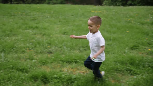 Boy Child Launches a Kite Running Through a Green Field in the Park in Summer