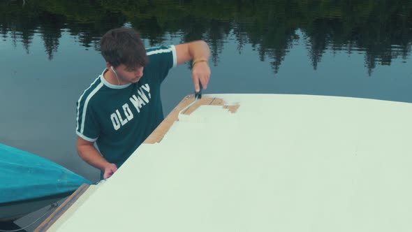 Young man finishes applying primer to wooden boat roof planks