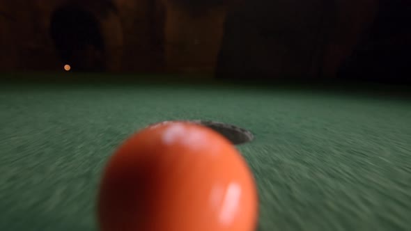 An orange mini golf ball falls into the golf hole and bounces in the pocket on a course.