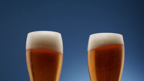 Two Glasses of Full Beer Collide in the Middle on a Blue Background