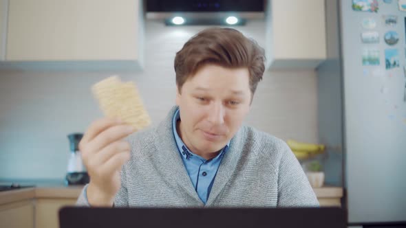 A Man Eats Bread While Working at a Laptop