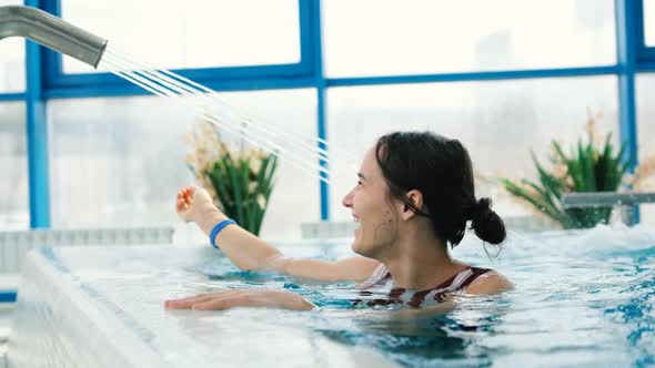 Attractive Young Woman Having Hydrotherapy in Luxury Pool Touching Water Stream with Hand and