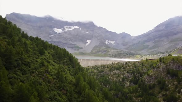 View of a dam in the swiss alps, next to a mountain lake. aerial shot, fir forest