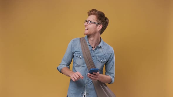 Happy Man on a Yellow Background with a Phone Points His Finger to the Side