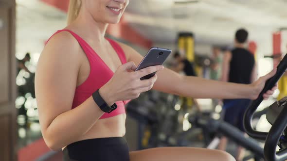 Athlete With Fitness Bracelet Riding Exercise Bike and Chatting on Cellphone