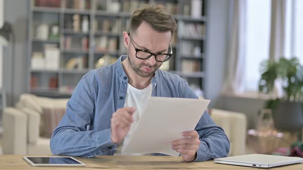 Hardworking Young Man Reading Documents in Loft Office