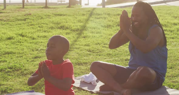 Video of african american father and son practicing yoga on grass on sunny day