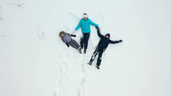 A Family with Children Makes a Figure of a Snow Angel in a Clearing in the Forest