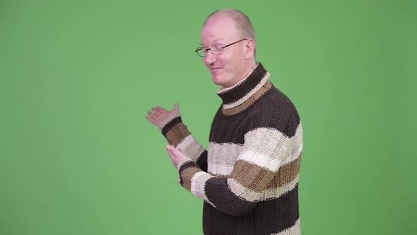 Happy Mature Bald Man with Turtleneck Sweater Showing Something