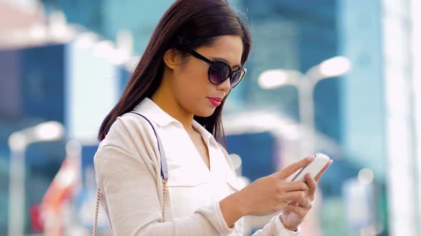 Asian Woman in Sunglasses Using Smartphone in City