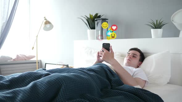 Young Man in Bed Watching a Live Stream on Smartphone Emoji and Likes