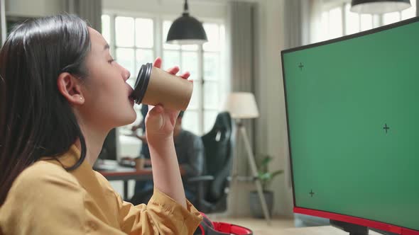 Asian Female Works And Drinking Coffee With Mock Up Green Screen Computer Display In Office