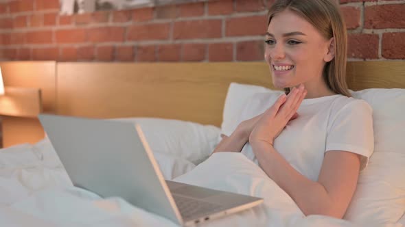 Cheerful Young Female Doing Video Chat on Laptop in Bed