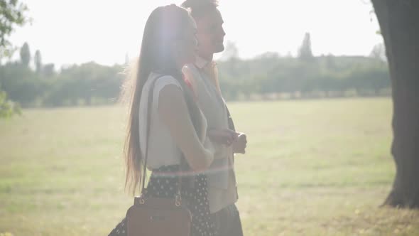 Side View of Young Couple Walking in Sunlight Outdoors and Talking. Happy Smiling Caucasian