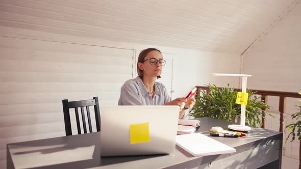 Woman Writing Notes Talking on Cellphone Remote Work From Home Office During Covid Lockdown