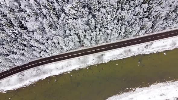 Aerial shot over a road and a river with a forest in winter