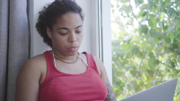 Portrait Adorable Young African American Woman Sitting on the Window Sill Typing on Her Laptop