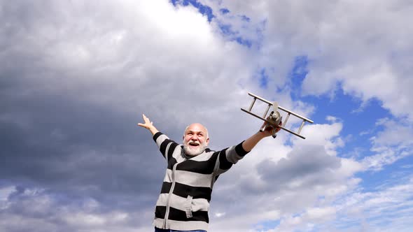 Happy Elderly Man Imagine Flying on Toy Airplane in Sky Dreaming