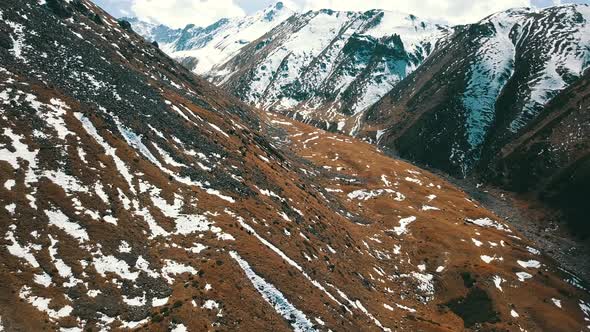 Mountain landscape with yellow grass. Peaks covered with snow. Flight on gorge 