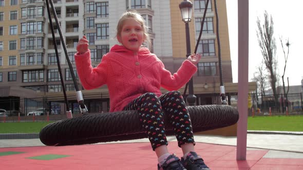 Junior Schoolgirl Sits on Swing Resting on Playground