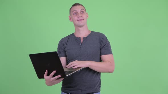 Happy Young Man Thinking and Using Laptop