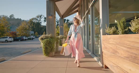 Attractive Stylish Woman in Pink Dress with Paper Bags Walking By Shopping Mall