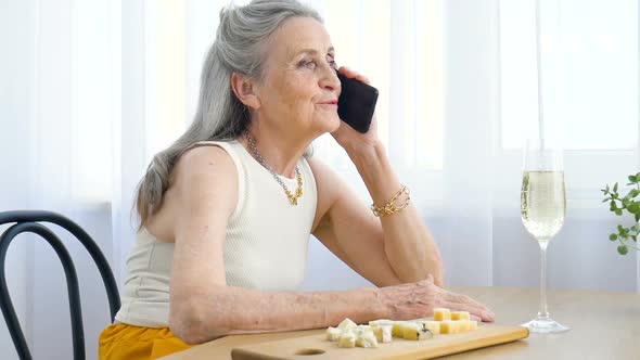 Beautiful Old Grandmother with Grey Hair and Face with Wrinkles is Using Smartphone Talking with