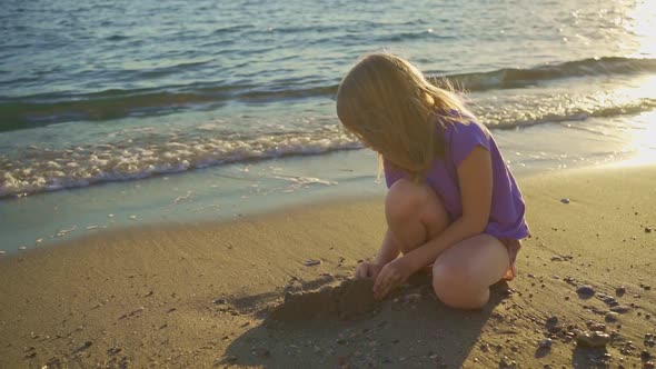 a Cute Little Girl Sits on the Seashore Playing in the Sand and with Pebbles