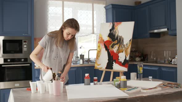 Female Artist Pouring Water before Drawing in Home Studio