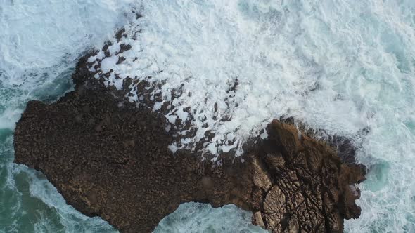 Large Ocean rock battered by waves in Praia Do Tonel, near Cape Sagres Portugal, Aerial rising shot