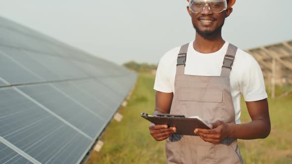 African American Man in Safety Glasses and Helmet Holding Clipboard While