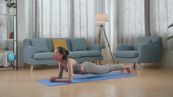 Young Asian Athletic Female In Sports Clothes Doing Yoga In Forearm Plank Pose On The Mat At Home