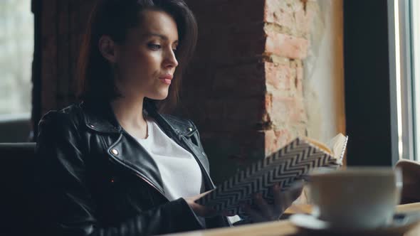 Attractive Girl Student Reading Book in Cafe Relaxing Sitting at Table Alone