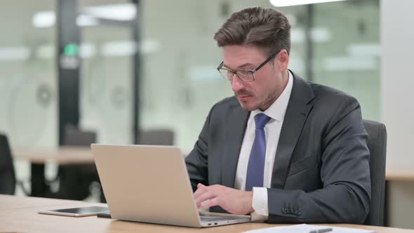 Middle Aged Businessman with Laptop Pointing at the Camera