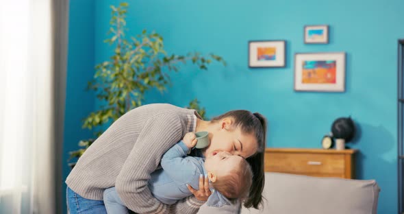 Happy Smiling Woman Spends Time in Living Room Holding Baby in Her Arms Leans Forward