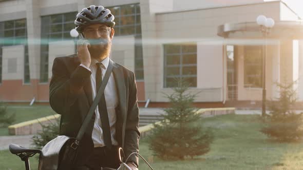 Business Man Talks on the Phone Wearing Bike Helmet at the Warm Sunset