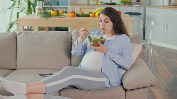 Pregnant Woman With Great Appetite Eats Vegetable Salad Lying on the Sofa