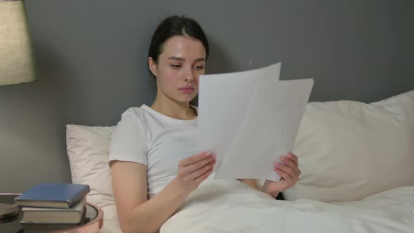 Young Woman Reading Documents in Bed 