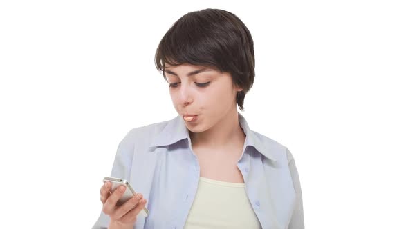 Lazy Caucasian Girl with Short Haircut Staring at Cellphone Chewing Gum and Blowing Bubbles
