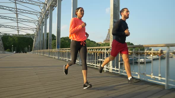 A man woman couple running across a bridge with the Eiffel Tower