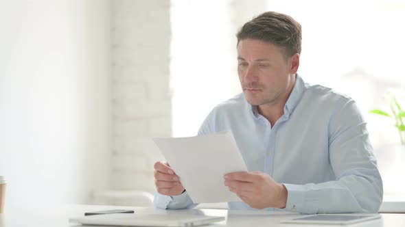 Man Reading Documents while Sitting in Office