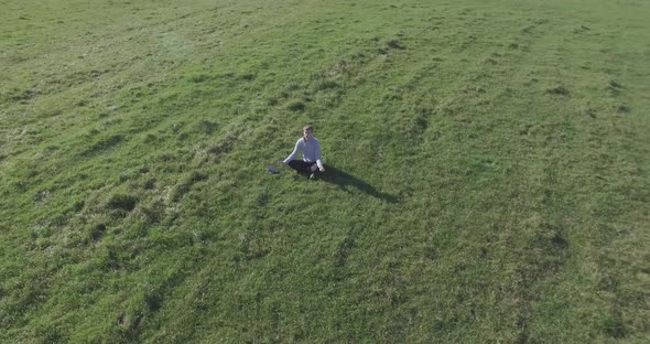 Low Orbital Flight Around Man on Green Grass with Notebook Pad at Yellow Rural Field